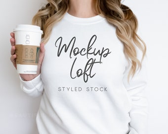 May include: A white sweatshirt with the text "Mockup Loft" and the words "Styled Stock" below it. A person is holding a coffee cup in their left hand.