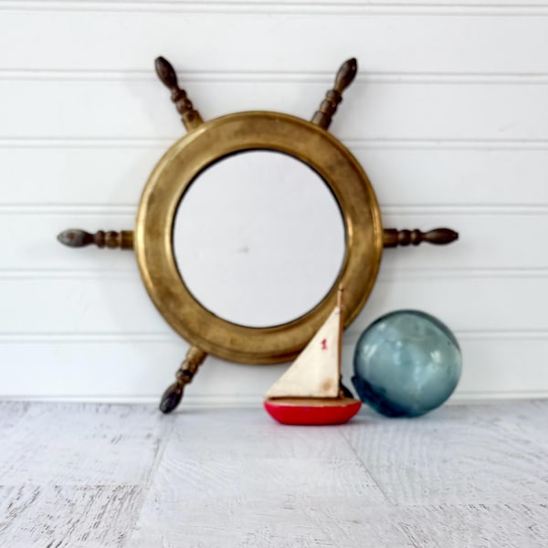 Espelho vintage em latão com roda de leme, pátina envelhecida em tons quentes, decoração costeira moderna.