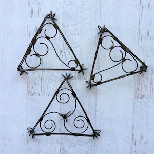May include: Three triangular metal trivets featuring a dark brown finish. Each piece is constructed from thin wire bent into a geometric triangle frame with internal decorative scrollwork and circular accents at the corners and center points.