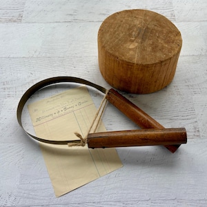 Könnte beinhalten: Ein vintage Zugmesser mit zwei Holzgriffen und einer gebogenen Metallklinge, begleitet von einem zylindrischen Holzblock und einem rechteckigen Papierbeleg mit dem Text "In account with Mrs. F. A. Stanton, Millinery & Fancy Goods."