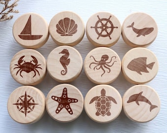May include: Twelve wooden cabinet knobs with nautical designs. Each knob features a different engraved image, including a sailboat, seashell, ship's wheel, whale, crab, seahorse, octopus, fish, compass, starfish, turtle, and dolphin.