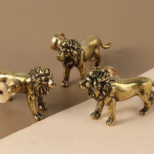 May include: Three gold lion-shaped cabinet knobs with a detailed design. The knobs are made of metal and have a polished finish.