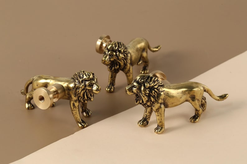 May include: Three gold lion-shaped cabinet knobs with a detailed design. The knobs are made of metal and have a polished finish.