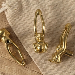 Op de afbeelding: Drie gouden, aapvormige kastknoppen. De apen staan in verschillende poses, één hangt ondersteboven, één zit en één staat.