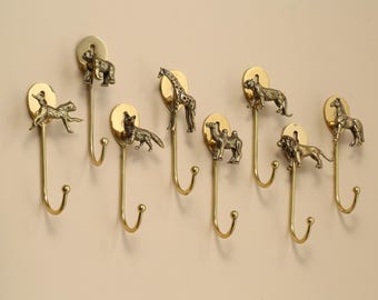 Peut inclure: Ensemble de neuf crochets muraux en laiton avec des animaux. Chaque crochet présente une figurine différente, comme un ours, un renard, une girafe, un chameau, un lion et un cheval. Fixés sur un mur clair.