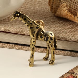 May include: A gold-toned giraffe figurine with a spotted pattern. The figurine is a decorative piece for a home or office.