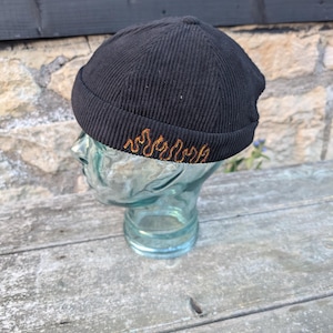 May include: Black corduroy beanie with a gold flame design.