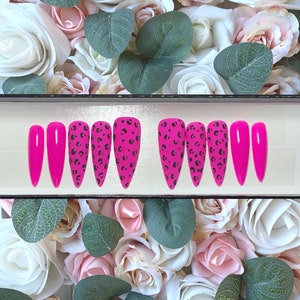 May include: A set of ten pink press-on nails with a leopard print design. The nails are in a box with a white background.