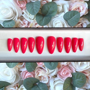 May include: A set of ten red almond-shaped false nails in a white box. The nails are arranged in two rows of five.