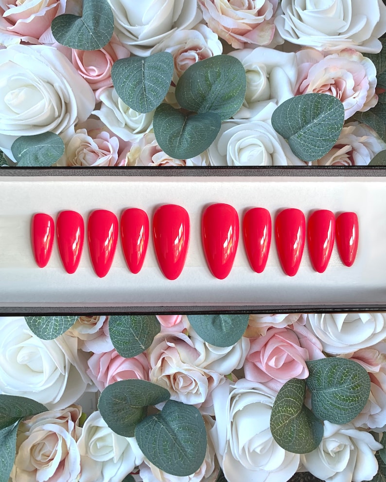 May include: A set of ten red almond-shaped false nails in a white box. The nails are arranged in two rows of five.