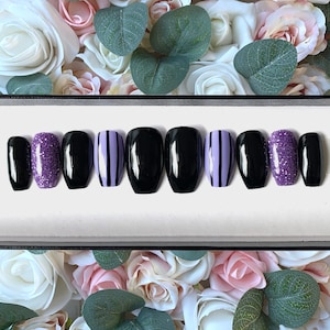 May include: A set of ten false nails in a black coffin shape. The nails are decorated with black and purple stripes, glitter, and solid black polish.