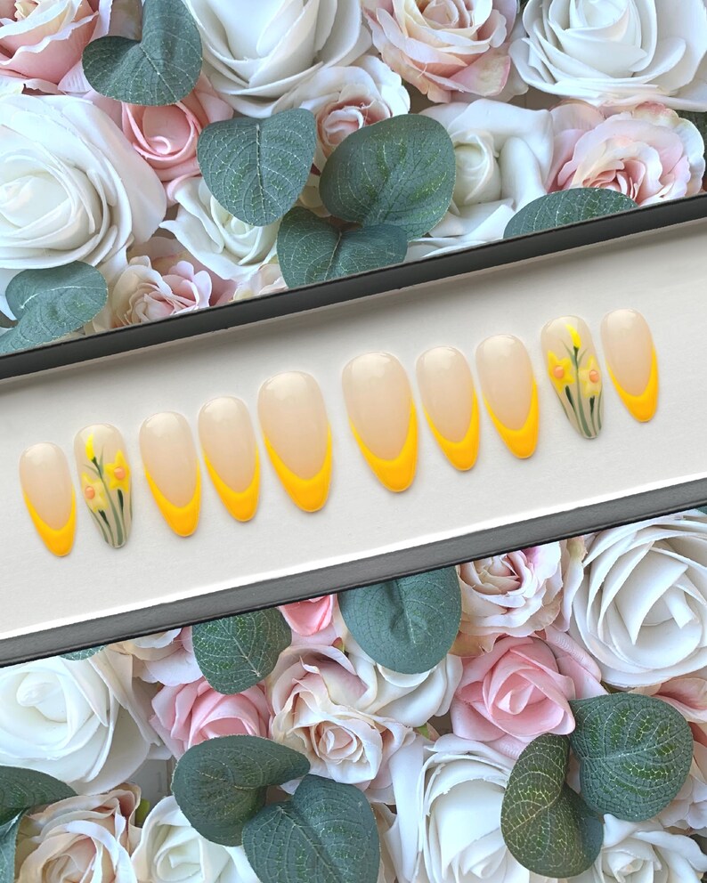 May include: A set of ten false nails with a yellow and white ombre design and a small floral design on one nail.