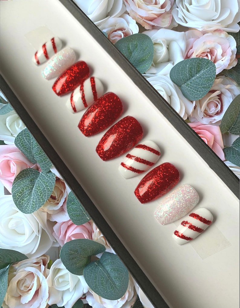 Puede incluir: Conjunto de diez u&ntilde;as postizas de tem&aacute;tica de bast&oacute;n de caramelo rojo y blanco. Las u&ntilde;as est&aacute;n decoradas con purpurina roja y rayas blancas.