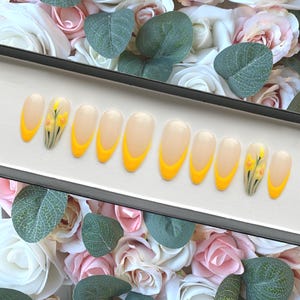 May include: A set of ten false nails with a yellow ombre design and a small floral design on the thumb nail.
