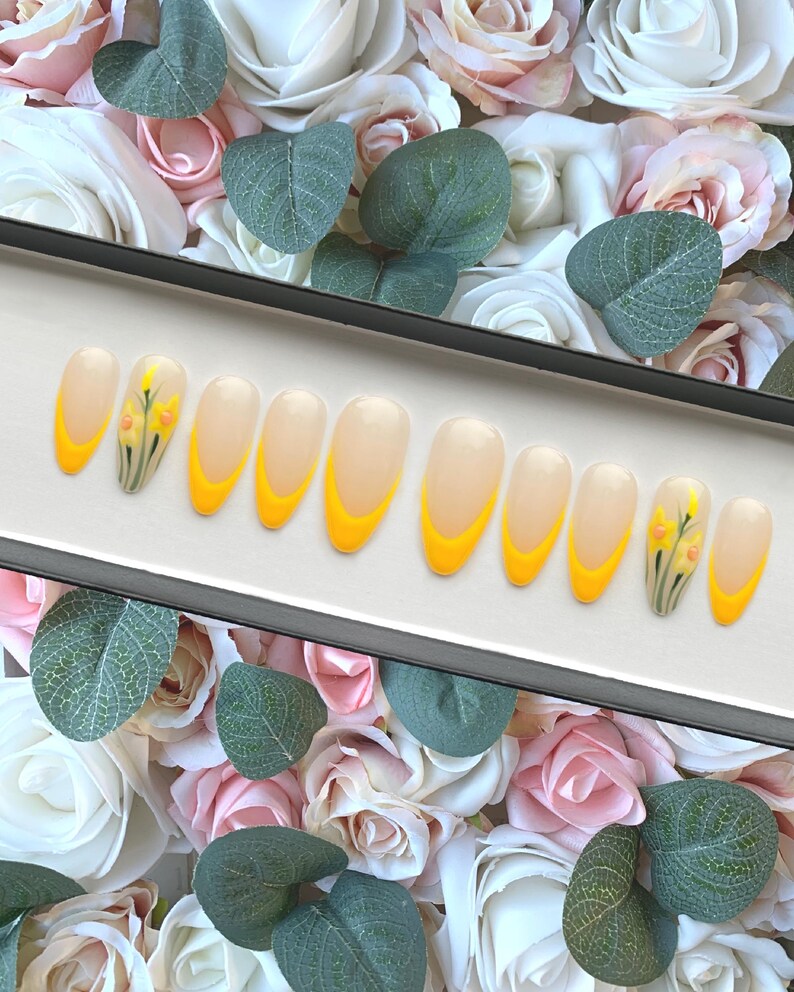 May include: A set of ten false nails with a yellow ombre design and a small floral design on the thumb nail.
