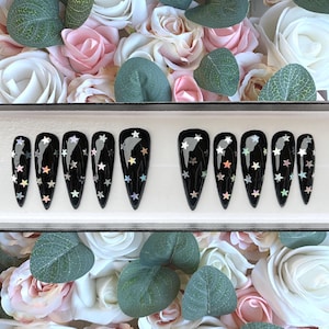 Puede incluir: Conjunto de diez uñas postizas negras con estrellas de purpurina iridiscente.