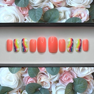 May include: A set of ten peach-colored press-on nails with rainbow and star designs. The nails are arranged in a row on a black background.