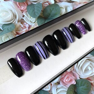 May include: Set of ten black coffin-shaped press-on nails with purple glitter and purple and black striped designs.
