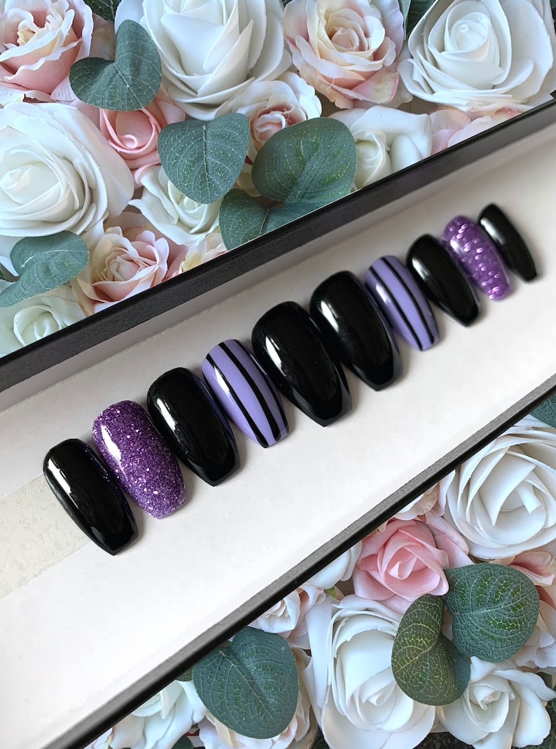 May include: Set of ten black coffin-shaped press-on nails with purple glitter and purple and black striped designs.