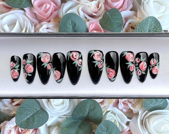May include: Set of ten black press-on nails with a floral design. Each nail is decorated with pink and green flowers.