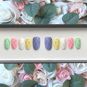 Può includere: Un set di dieci unghie finte con un designo maculato in colori pastello, tra cui verde, rosa, giallo, viola e bianco. Le unghie sono disposte in una scatola con sfondo bianco.