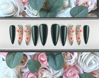 May include: A set of ten dark green, almond-shaped, long false nails with a floral design. The design features small red berries and white leaves on a light pink background.