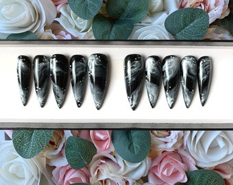 May include: Set of ten black and white swirl nail tips with white glitter accents. The tips are arranged in two rows of five on a white surface.