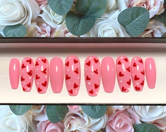 May include: Set of ten pink oval-shaped press-on nails with a white base and red heart designs.