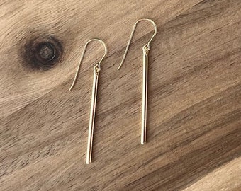 May include: A pair of gold-toned dangle earrings with thin, straight bars hanging from the hooks.