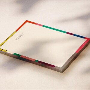 May include: A rectangular notepad with cream-colored paper featuring the word NOTES printed in black. The border is decorated with colorful geometric segments in red, green, blue, pink, and a yellow strip with black polka dots along the left side.