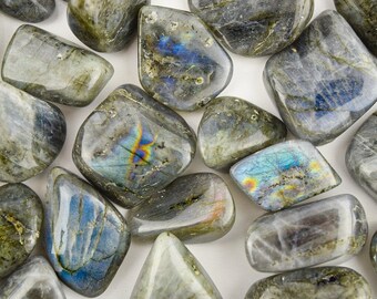 May include: A collection of tumbled labradorite stones. The stones are a mix of gray, blue, and green with iridescent flashes of color.