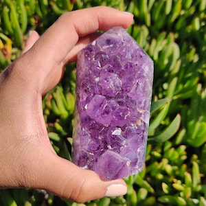 May include: A large, purple amethyst crystal cluster in the shape of a point. The crystal is made up of many smaller, faceted crystals that are clustered together.