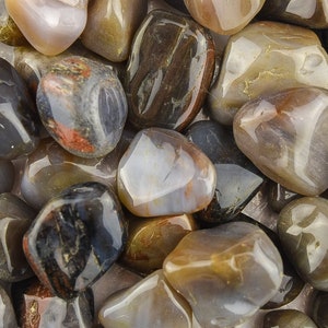 May include: A collection of polished gemstones in various shades of brown, gray, and tan. The stones have a smooth, glossy surface with natural patterns and variations in color, creating a visually appealing texture. The gemstones are tumbled and appear to be of various sizes.