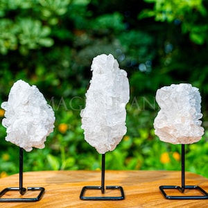 May include: Three white crystal clusters on black metal stands. The crystals are arranged in a row on a wooden surface.