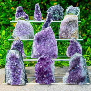 May include: A collection of amethyst crystals of various sizes and shapes, displayed on a tiered stand. The crystals are a deep purple colour and have a natural, rough texture.