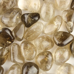 May include: A collection of tumbled smoky quartz stones. The stones are a light brown color and have a translucent appearance. They are smooth and polished, with a natural, irregular shape.