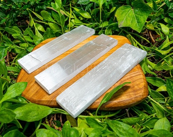 May include: Three white selenite charging wands on a wooden surface. The wands are smooth and have a natural, crystalline texture.