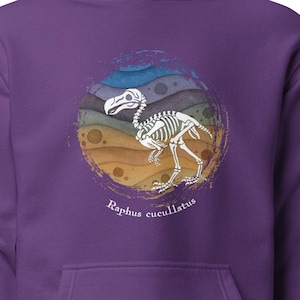Könnte beinhalten: Ein lila Kapuzenpullover mit einer Grafik eines Dodo-Vogelskeletts in einem farbenfrohen kreisförmigen Design. Der Text "Raphus cucullatus" ist darunter aufgedruckt. Der Pullover hat eine Kängurutasche und eine Kapuze mit Kordelzug.
