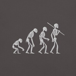 May include: An embroidered design on a dark gray background depicts the evolution of a skeleton. The progression shows a skeleton in a hunched position, gradually becoming upright, with the final skeleton carrying a stick over its shoulder.