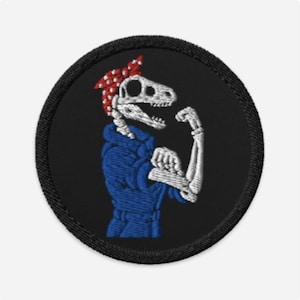 May include: Embroidered patch showing a dinosaur skeleton flexing its arm. The skeleton wears a blue jumpsuit and a red and white polka-dot bandana. The patch is round with a black background and a black stitched border.