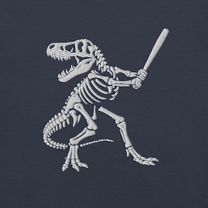 May include: White embroidered image of a Tyrannosaurus Rex skeleton in a baseball stance, holding a bat. The dinosaur is crouched low, ready to swing. The background is a solid navy blue.