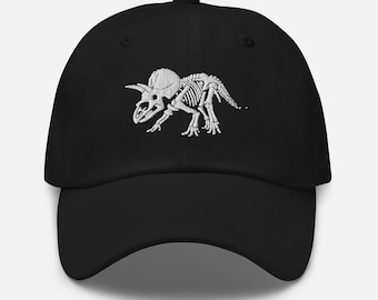 May include: Black baseball cap featuring a white embroidered Triceratops skeleton design. The cap has a curved brim and an adjustable strap at the back. A stylish accessory for dinosaur enthusiasts.