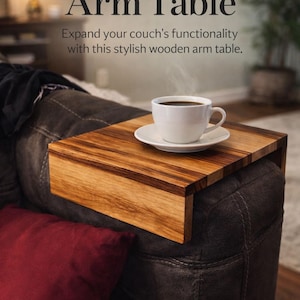 May include: A wooden arm table with a striped pattern, resting on a dark brown leather couch. A white cup of coffee sits on the table. The text reads "The Perfect Arm Table".