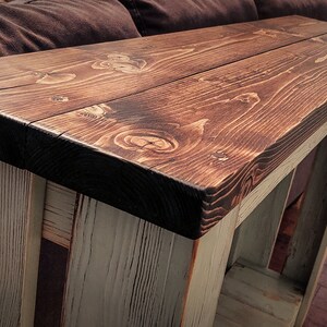 May include: A rustic wooden console table with a dark brown stained top and a whitewashed base. The table has a simple design with a rectangular top and four legs.