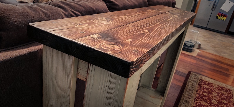May include: A rustic wooden console table with a dark brown stained top and a whitewashed base. The table has a simple design with a rectangular top and four legs.