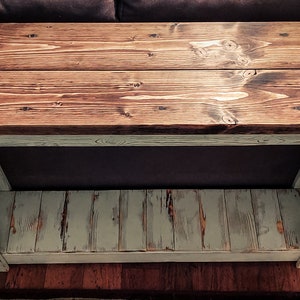 May include: A rustic wooden console table with a distressed white finish. The top is made of two planks of wood with a natural wood stain. The bottom shelf is also made of wood and has a distressed white finish.