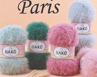 May include: A collection of fluffy yarn balls in shades of pink, green, and blue-grey, with the word "Paris" above. Each ball has a label that reads "NAKO Paris". Two wooden knitting needles are in the foreground.