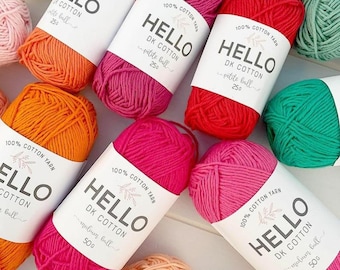 May include: A collection of colorful yarn balls in shades of orange, pink, red, and green. Each ball is wrapped with a white label that reads "HELLO DK COTTON". The yarn is 100% cotton and available in petite and medium ball sizes.