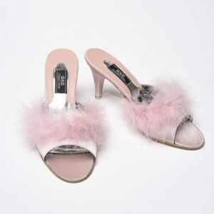 May include: A pair of pink satin heeled slippers with a fluffy pink feather trim. The slippers have a black label that reads "G&C Collection".