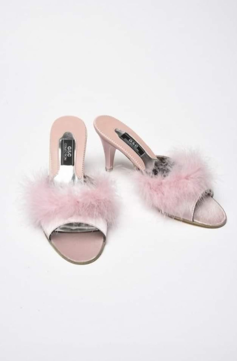 May include: A pair of pink satin heeled slippers with a fluffy pink feather trim. The slippers have a black label that reads "G&C Collection".